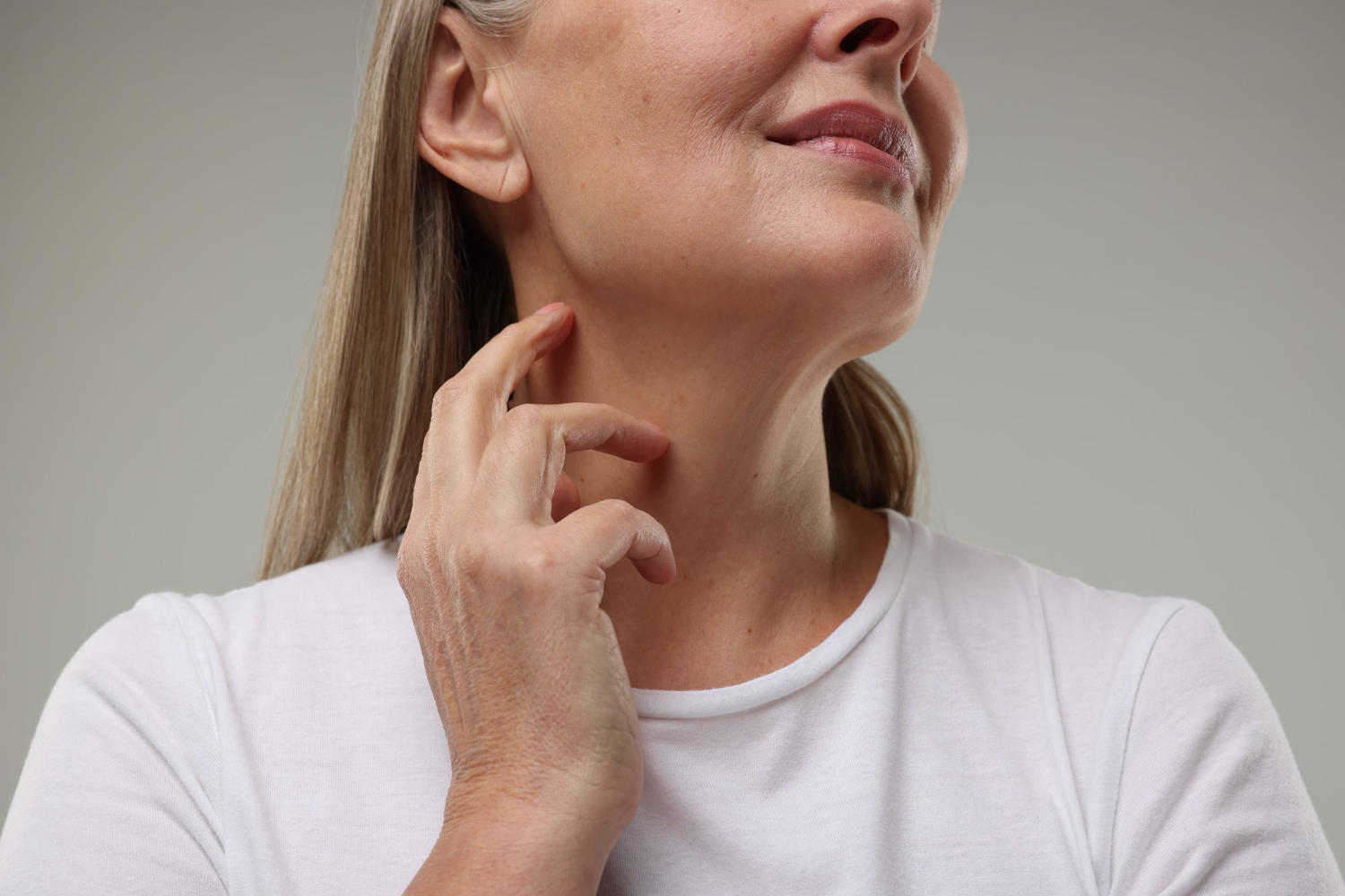 Mulher toca a região do pescoço, destacando flacidez e sinais de envelhecimento facial.