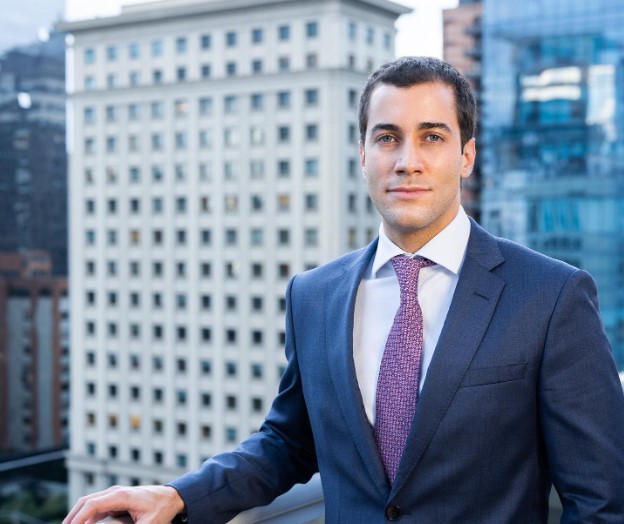 Dr. João Carlos, cirurgião plástico, em retrato profissional com prédios urbanos ao fundo.