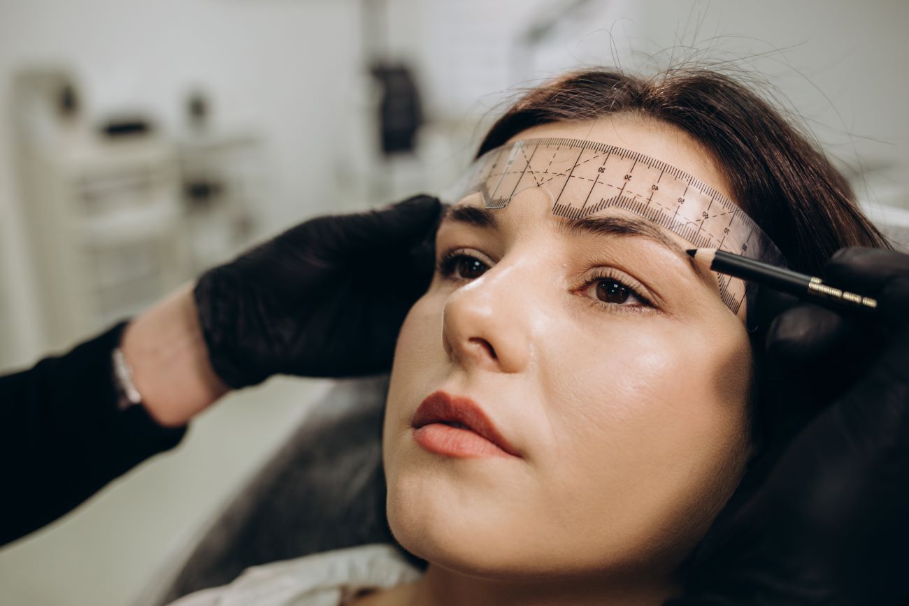 Mulher deitada, com profissional marcando sua testa e sobrancelha para cirurgia.