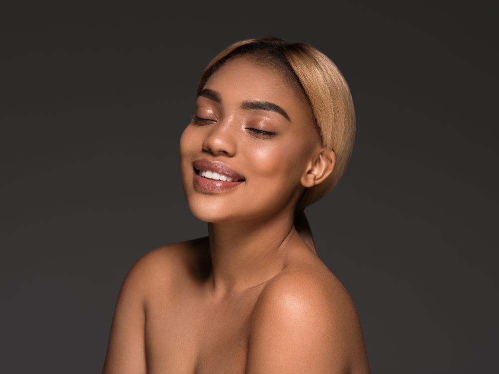 Mulher jovem de olhos fechados e sorriso suave, com pele facial luminosa e contornos harmônicos, ilustrando os resultados naturais da lipoenxertia facial.
