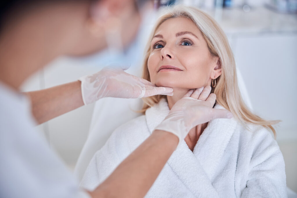 Médico avalia a região do pescoço e do rosto de uma paciente durante consulta estética em clínica.