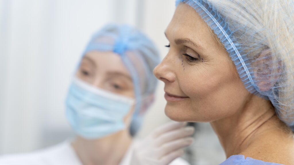 Cirurgião plástico com máscara e luvas examina o rosto de paciente madura com marcações cirúrgicas próximas aos olhos, em preparação para procedimento de rejuvenescimento facial.